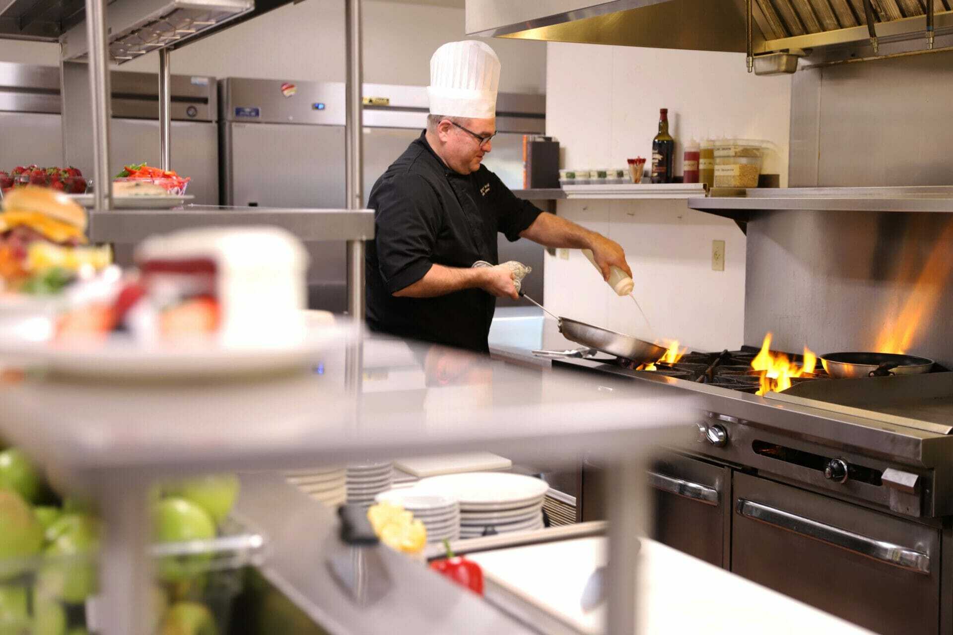 Chef spraying oil into pan on oven.