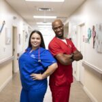 A nurse and CNA standing back to back.