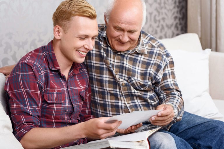 Son and elderly father taking part in memory care activities by looking through photos