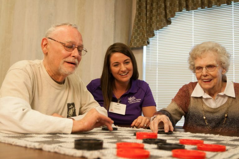 elderly man and woman playing checkers with care assistant